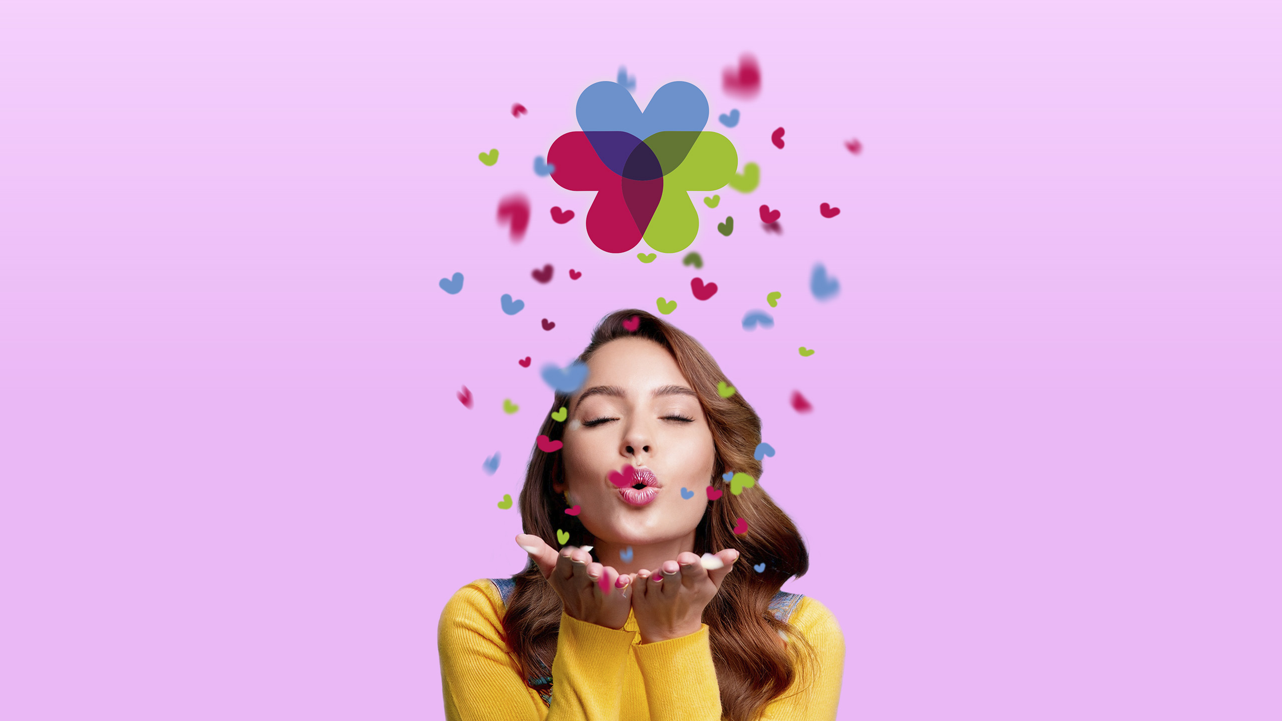 Chica soplando miles de confeti de colores con forma de corazón y que forman el logo de Penedès Village